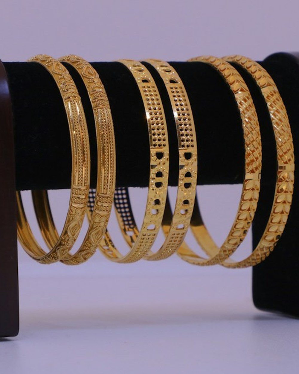 Photorealistic concept visual of traditional engraved gold-toned bangles stacked on a display stand. Illustrative design reference only, not current shop stock.
