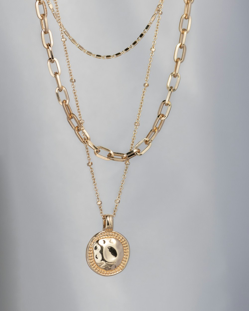 Photorealistic concept visual of layered gold chains with a relief coin medallion pendant. Illustrative design reference only, not current shop stock.